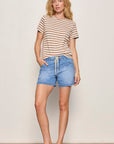 Woman wearing a striped shirt and denim shorts against a plain background