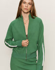 Woman wearing a green tracksuit with white stripes on a plain background