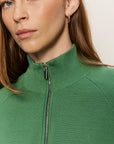 Close-up of a person wearing a green zip-up sweater against a neutral background