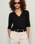 Person wearing a black shirt and beige pants with sunglasses on a plain background