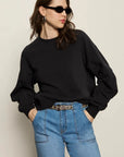 Woman wearing a black sweater and blue jeans against a plain background