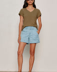 Woman wearing an olive green t-shirt and light blue shorts against a plain background