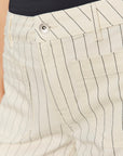 Close-up of beige pants with black vertical stripes and a button.
