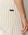 Close-up of a person wearing beige pinstripe pants with a visible brand label, on a neutral background.