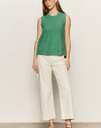 Woman wearing a green sleeveless top and white pants against a plain background