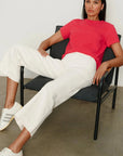 Woman sitting on a chair wearing a red shirt and white pants with Adidas shoes.