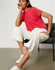 Woman sitting on a chair wearing a red shirt, white pants, and white sneakers.