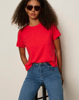 Person wearing a red t-shirt and blue jeans with sunglasses on a plain background