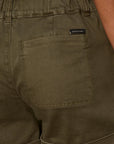 Close-up of olive green shorts with a brand label on the pocket.