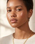 Woman wearing a gold necklace against a neutral background