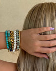 Person with long blonde hair and colorful bracelets on a beige background