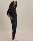 Woman wearing a navy tracksuit with white sneakers on a beige background