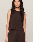 Woman wearing a brown sleeveless top and pants against a neutral background