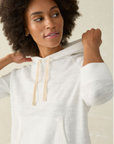 A female model wearing a white slub knit hoodie with a drawcord at the hood and a kangaroo pocket, paired with blue denim shorts.