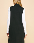 A woman shown from the back wearing a black sleeveless mock-neck longline vest over a white long-sleeve shirt, set against a solid beige background.