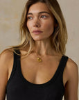 Woman wearing a black tank top and gold necklace against a beige background