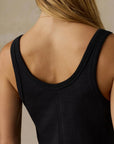 Close-up back view of a woman wearing a black ribbed tank top against a neutral beige background.