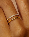 Close-up of a hand wearing two gold rings with diamond accents on a beige background