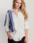 Woman wearing a white striped shirt with rolled-up sleeves, holding a blue towel over her shoulder against a plain background.