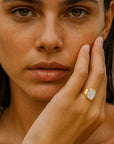 Woman with a gold ring on her finger touching her face outdoors