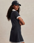 Woman wearing a navy dress and cap with a logo on a beige background