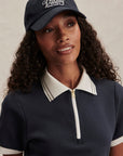 Woman wearing a navy cap and matching polo shirt with white accents on a neutral background