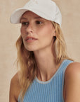 Woman wearing a white cap and blue tank top against a beige background