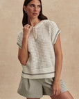 Woman wearing a white patterned top and beige shorts against a beige background