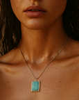 Close-up of a person wearing a gold necklace with a turquoise pendant against a neutral background