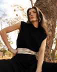 Woman in a black dress with a silver belt sitting against a tree