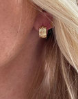 Close-up of a gold earring worn in an ear with blonde hair.