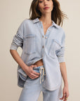 Woman wearing a light blue denim shirt and pants against a beige background