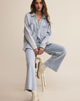 Woman sitting on a stool wearing a light blue denim outfit against a beige background