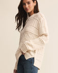 Woman wearing a cream knitted sweater and blue jeans on a beige background