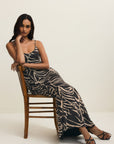 Woman sitting on a wooden chair wearing a patterned dress against a plain background