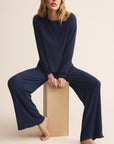 Woman wearing a navy blue ribbed outfit sitting on a wooden block against a beige background