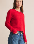 Woman wearing a red sweater and blue jeans against a beige background