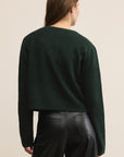 Person wearing a dark green sweater and black pants on a beige background