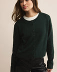 Woman wearing a dark green cardigan over a white shirt on a beige background