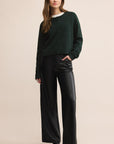 Woman wearing a dark green sweater and black pants on a beige background