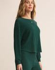 Woman wearing a green ribbed sweater and pants on a beige background