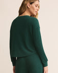 Woman wearing a green ribbed sweater and pants on a beige background
