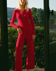 Woman in a bright pink outfit standing on a balcony with greenery in the background