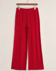 Red pants hanging on a wooden hanger against a white background