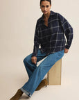 Woman wearing a plaid shirt and blue jeans sitting on a wooden block against a beige background