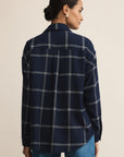 Woman wearing a navy plaid shirt and blue jeans on a beige background