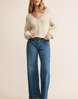 Woman wearing a cream cardigan and blue jeans on a beige background