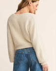 Woman wearing a cream sweater and blue jeans on a beige background