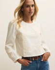 Woman wearing a white blouse with lace details and blue jeans against a plain background