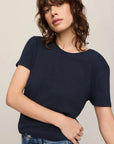 Woman wearing a navy blue t-shirt and blue jeans against a plain background